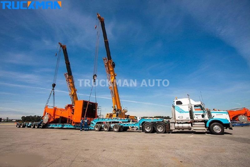 Deux grues mobiles soulevant du matériel lourd sur une semi-remorque surbaissée
