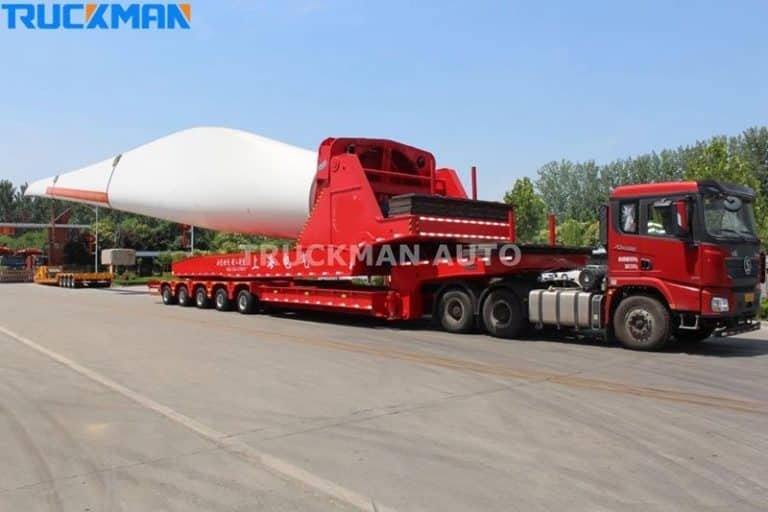 Semi-remorque surbaissée chargée de longues pales d'éoliennes blanches, d'une grande capacité de travail.